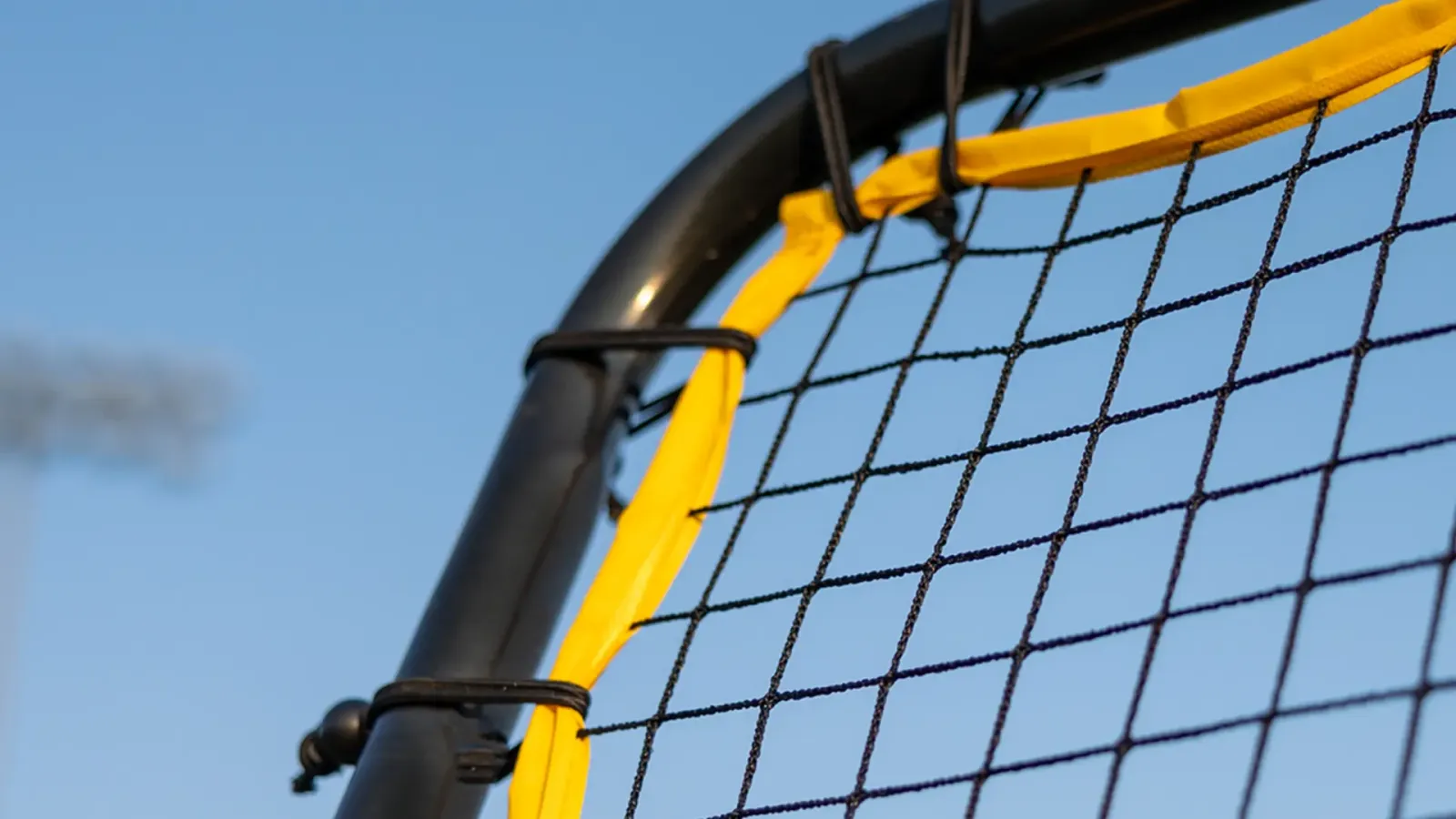 Lacrosse goal corner with a yellow shot trainer strap against a blue sky