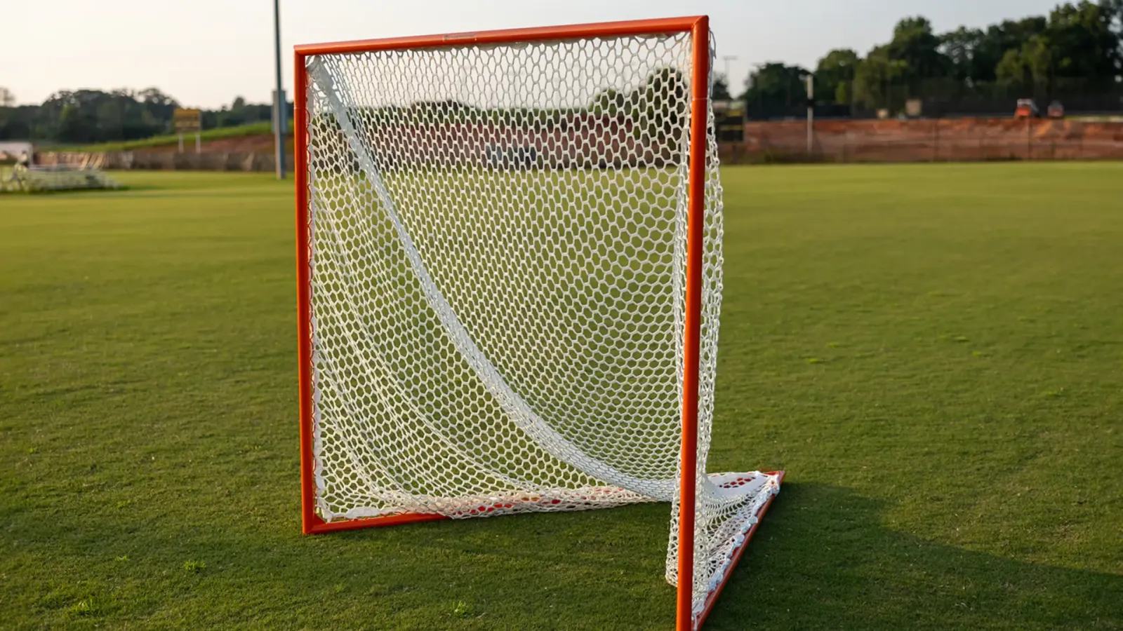 Orange Crankshooter lacrosse goal with a white net on a grass field